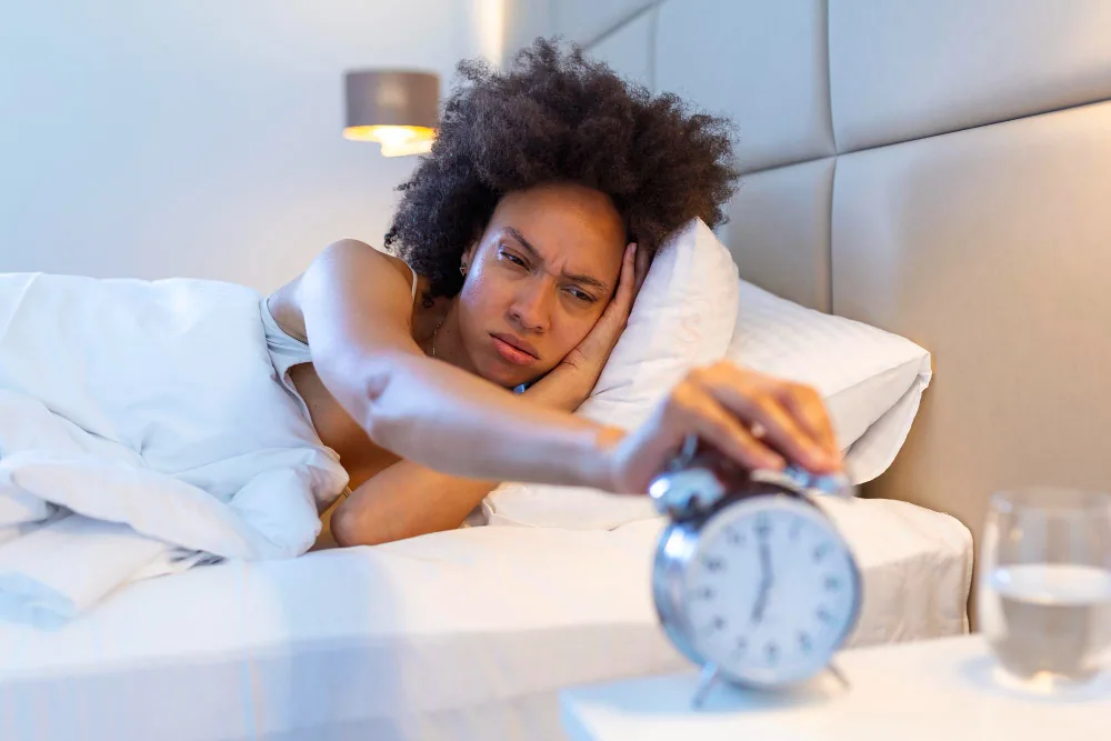 Woman lying awake beside an alarm clock during a persistent episode of insomnia